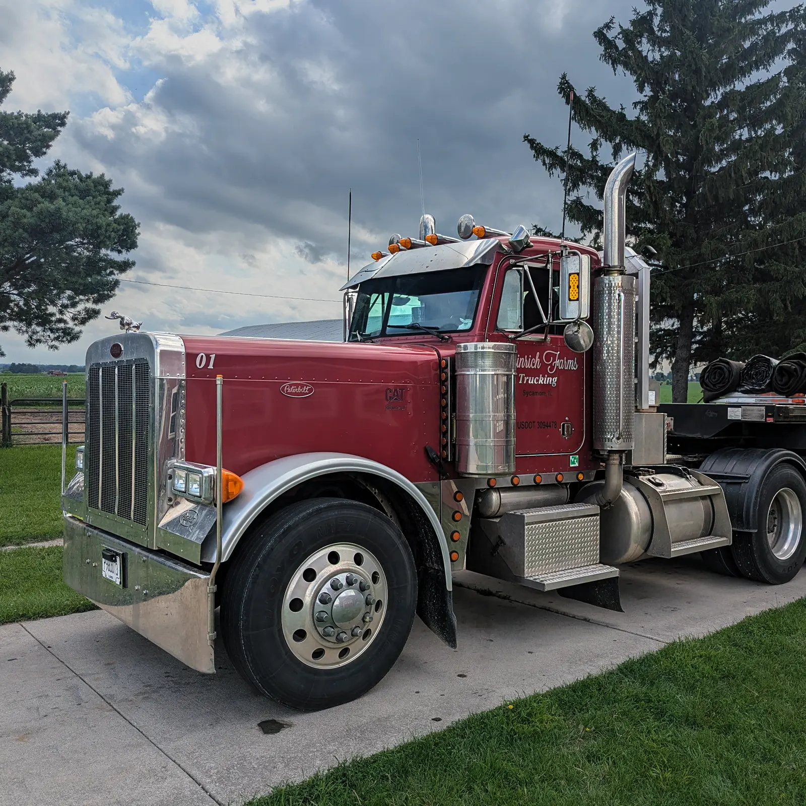 A maroon Heinrich Farms Trucking Peterbilt semi truck parked beside a farm field in Sycamore, Illinois